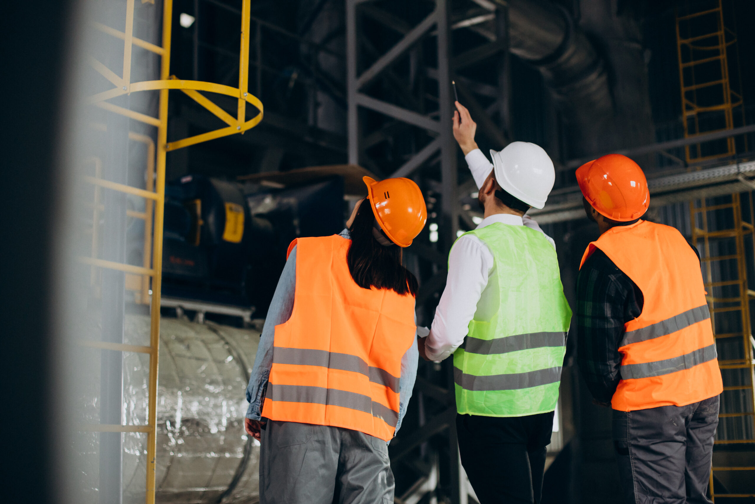 three factory workers in safety hats discussing manufacture plan